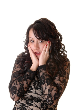 A really scared young woman holding her face in her hands, with longblack curly hair in a black lace dress for white background.の写真素材