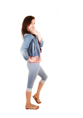 A young beautiful woman in thighs and a jeans jacket walking in the studio for white background whit her long brunette hair の写真素材