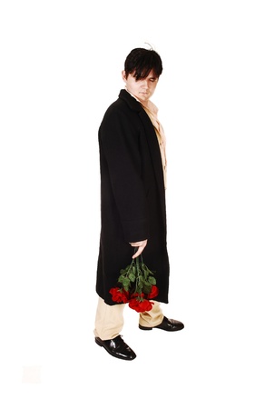 A young man in a beige suit and black coat with a bunch of red roses inhis hand, standing for white background, is sad of broken relationship の写真素材