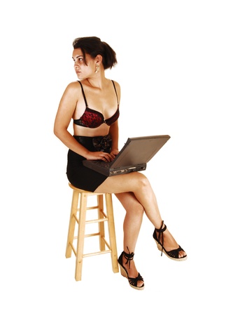 A pretty, young woman with a laptop on her lap, sitting on a chair in ablack skirt and black red bra with legs crossed for white background,looking back  の写真素材