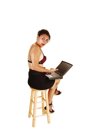 A pretty young woman with a laptop on her lap, sitting on a chair in ablack skirt and black red bra with legs crossed for white background の写真素材