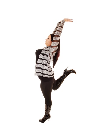 A pretty woman with a full figure standing for white background in tightsand black boots, stretching her arms above her heat, showing her figure の写真素材