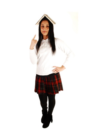 A lovely teenage girl in her school uniform with a book on top of her headstanding for white background with her long black hair の写真素材