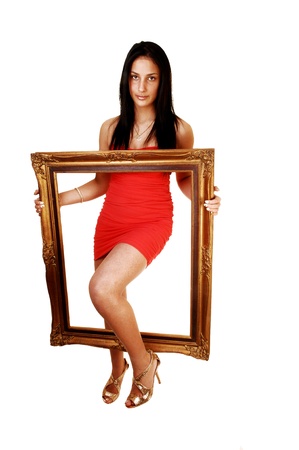 A lovely young teen girl in a red dress and gold high heels, with her longblack hair stepping trough a picture frame for white background の写真素材