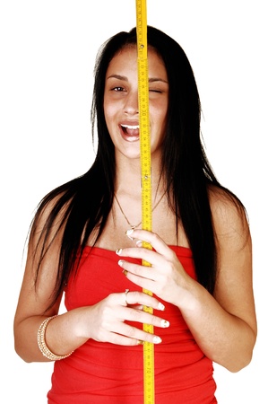 A pretty and laughing teen girl standing for white background and holdingup a yellow measuring stick for her face の写真素材