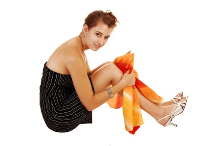 A pretty and young woman in a black dress with striped on sitting fromthe side for white background on the floor の写真素材