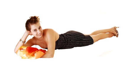 A pretty and young woman in a black dress with stripes on lying in frondon her stomach for white background with a colourful scarf の写真素材
