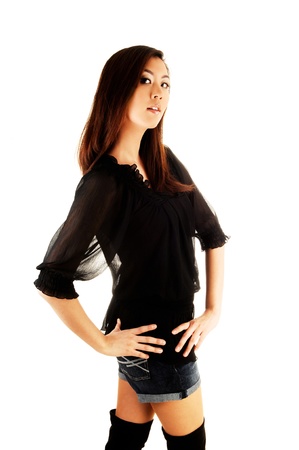 A tall and pretty chinese woman in a black blouse and long black bootsstanding in the studio for white background の写真素材