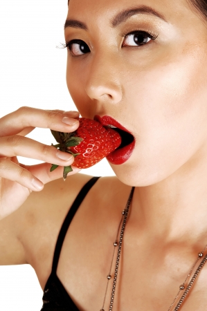 A closeup of a young pretty chinese woman, eating a big strawberrylooking into the camera for white background の写真素材