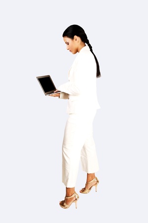 A young business woman with a laptop in her hands standing for light bluebackground in a white suit and high heels and a ponytail の写真素材