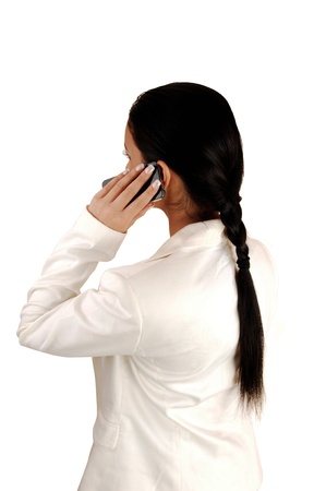 A young business woman standing from the back in a white suit with herblack ponytail, talking on her cell phone for white background の写真素材