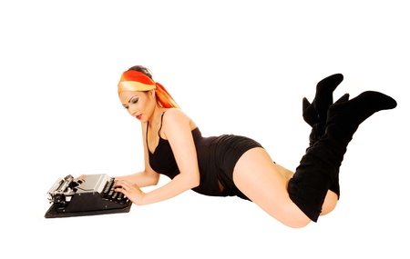 A pretty girl in black shorts and long boots lying on the floor for whitebackground and typing on an old typewriter の写真素材