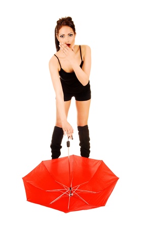 A young woman in black shorts and long boots standing with a red umbrellaon the floor is looking very surprised for white background の写真素材