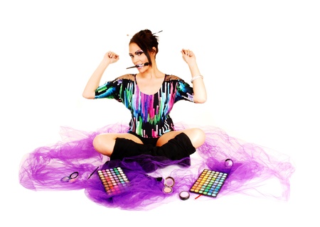 A young woman sitting on lilac twill on the floor with crossed legs and blacklong boots putting on her makeup, holding up her hands の写真素材