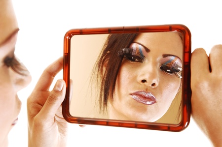 A young pretty woman holding up a mirror looking at her makeup with longeyelashes and nice makeup for white background の写真素材