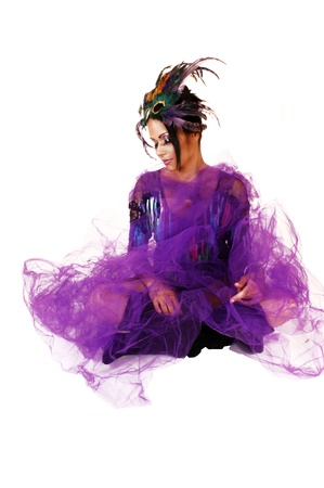 A young woman sitting on lilac twill on the floor with crossed legs and blacklong boots with a feather mask on her forehead の写真素材