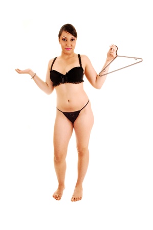 A young woman standing in black underwear with an empty cloth hanger inher hand for white background and dos not know what to wear の写真素材