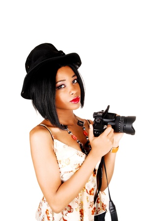 A lovely young woman with a black hat and a camera in her hand standingfor white background ready to take some pictures の写真素材