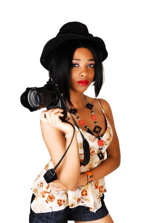 A young lovely and serious woman standing for white background with ablack hat and holding a camera in her hand の写真素材