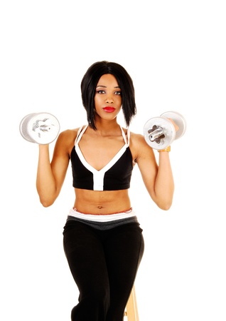 A slim young woman in black exercise clothing working out with silvercolor dumbbells for white background の写真素材