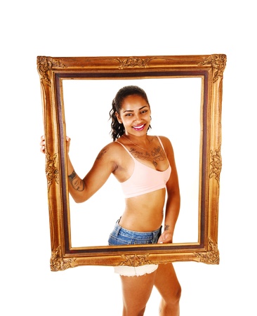 A smiling pretty young woman in shorts and exercise bra standing forwhite background holding a big picture frame in front of her の写真素材