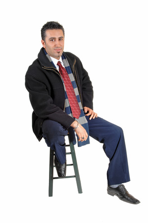 A tall and young businessman sitting on a chair in a black coat forwhite background relaxing の写真素材