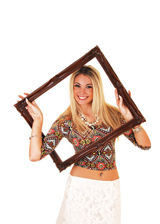 A smiling blond woman holding up a picture frame and looking trough,for white background の写真素材
