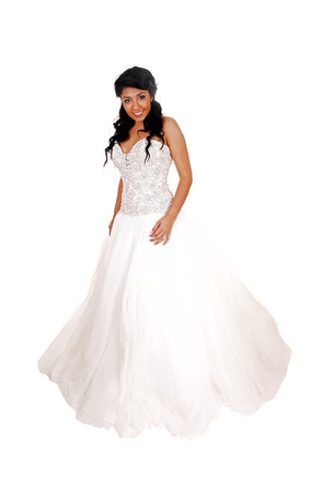 A lovely young woman with long curly black hair standing in her white weddingdress for white background の写真素材