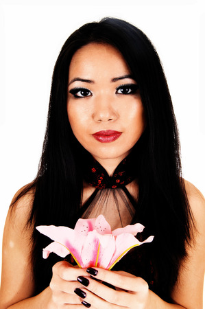 A beautiful young Chinese woman with long black hair in a portrait pictureholding a pink lily for white background の写真素材