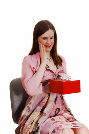 A young pretty woman sitting on a chair in a nice dress getting a redgift box for white background の写真素材