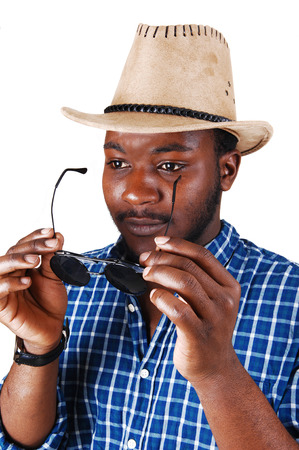 A serious looking black man in a portrait picture with a cowboy hat, holdinghis sunglasses, isolated for white background の写真素材