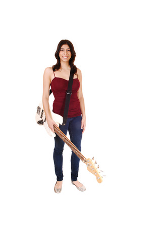 A lovely slim woman standing in jeans and a burgundy t-shirt, holdingher guitar and smiling, isolated on white background の写真素材
