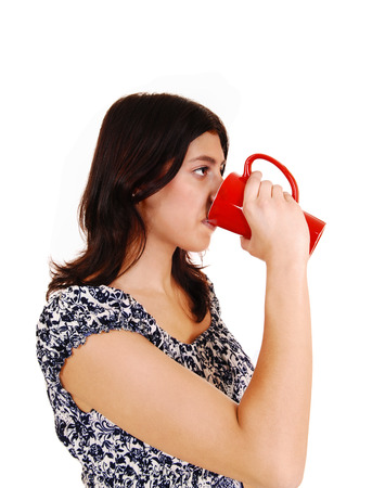 A young brunette woman in a dress drinking coffee from a red mug,isolated on white background の写真素材