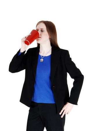 A young woman in a black suit drinking coffee from a red mugisolated for white background の写真素材