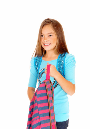 A pretty eight year old girl is looking and holding her backpack in a closeuppicture, isolated on white background.の写真素材