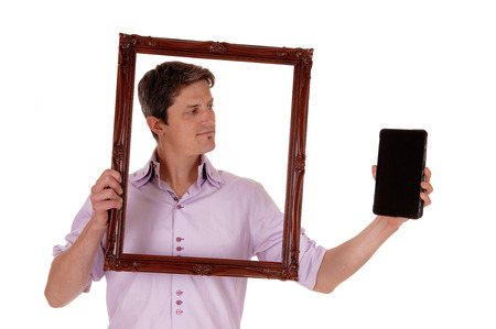 A young man holding up a picture frame, looking trough on his tablet,
isolated for white background.の写真素材