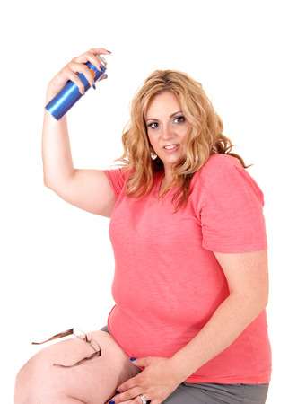 A lovely plus size woman sitting in shorts on a chair and spraying hair
spray on her hair, isolated foe white background.の写真素材