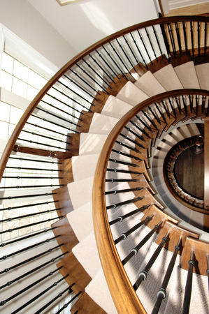 A beautiful round staircase in a closeup picture over three floors in oakwood with carpet and a window on the left.の写真素材