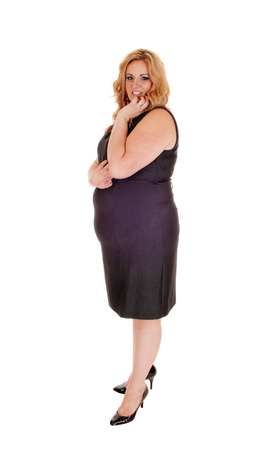 Plus size young woman standing isolated for white background with
her hand on her chin, in high heels and a gray dress.の写真素材