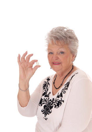A beautiful senior woman in her seventies holding a vitamin pill, in closeup
isolated for white background.の写真素材