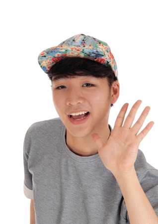 A happy Asian teenager in a closeup image waiving his hand, wearing
a cap on his head, isolated for white background.の写真素材