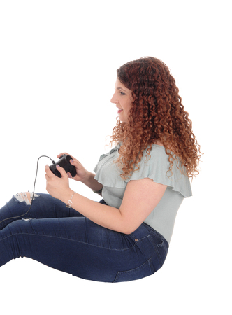 A young woman sitting on the floor, holding her console and playinga video game, isolated for white...