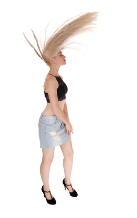 A beautiful slim blond woman flying her long hair over her head,
standing in a jeans skirt and black bra, isolated for white backgroundの写真素材