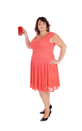 An overweight woman in a red dress standing in profile with a necklace
and holding a red coffee mug, isolated for white background
の写真素材