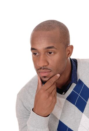 A young handsome African American man sitting in the studio with 
one hand on his chin, thinking, isolated for white background
の写真素材
