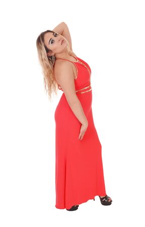Lovely young woman standing in a long red evening dress in profile
with one hand behind her head, isolated for white backgroundの写真素材
