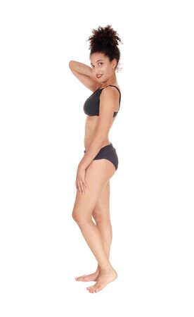 A beautiful slim young multi-racial woman standing in profile in a black
bikini in the studio looking into camera, bare foot with her curly black 
hair in a bun on her head, isolated for white backgroundの写真素材