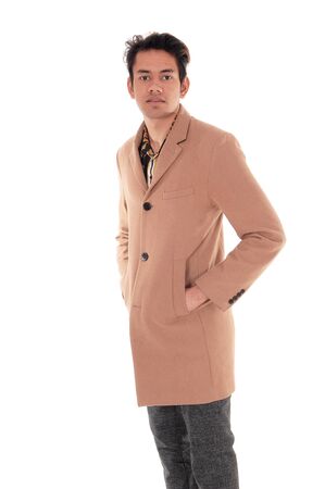A tall young man standing in a beige coat in profile in the studio
looking at the camera, isolated for white backgroundの写真素材