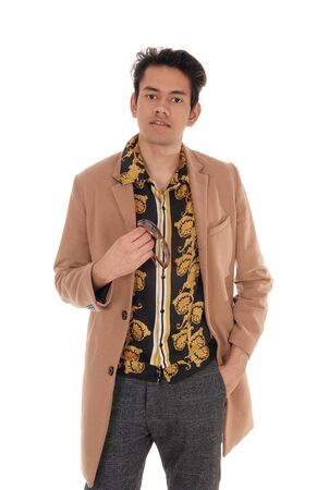 A tall handsome young man standing in a beige coat and gray pants,
holding his sunglasses in his hand, isolated for white backgroundの写真素材