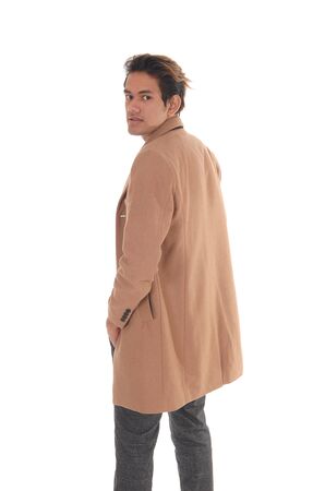 A tall young man standing in a beige coat from the back in the studio
looking over his shoulder, isolated for white backgroundの写真素材